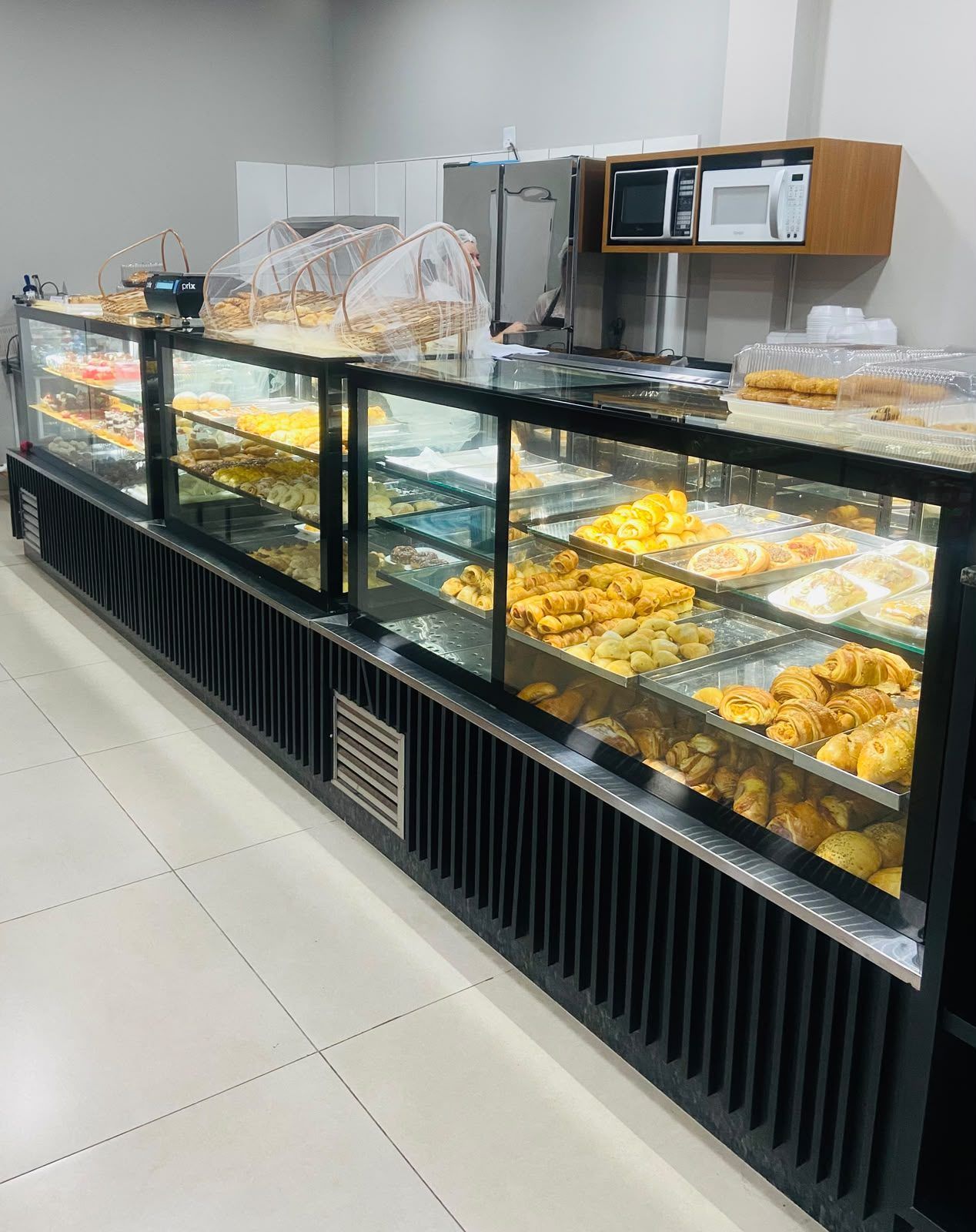 Vitrine refrigerada preta com prateleiras de vidro exibindo doces e tortas em confeitaria