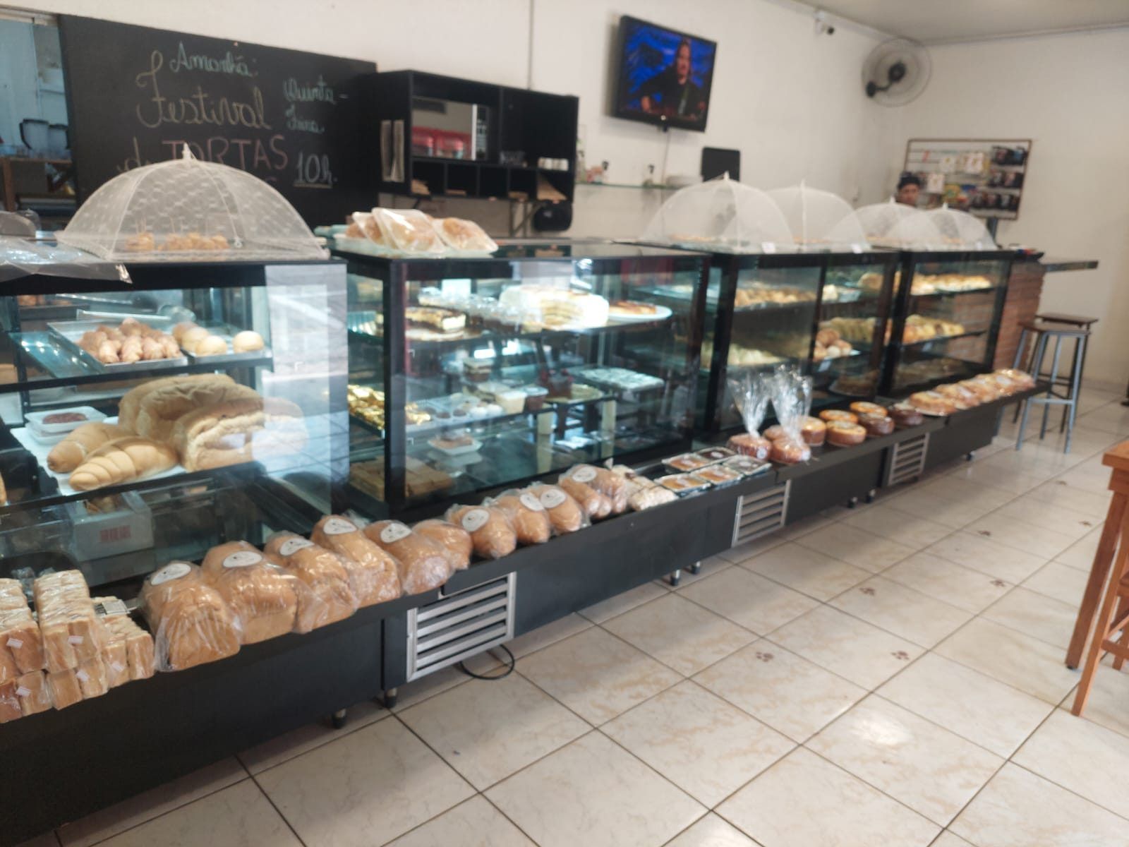 Vitrine refrigerada com vidro curvo exibindo bolos e doces no balcão de atendimento da padaria